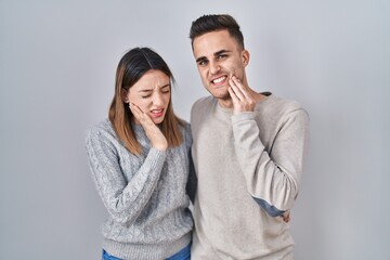 Young hispanic couple standing over white background touching mouth with hand with painful expression because of toothache or dental illness on teeth. dentist concept.
