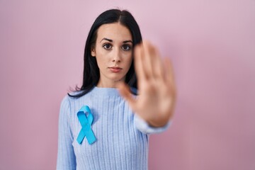 Hispanic woman wearing blue ribbon with open hand doing stop sign with serious and confident expression, defense gesture