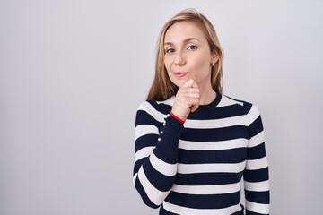 Young caucasian woman wearing casual navy sweater looking confident at the camera with smile with crossed arms and hand raised on chin. thinking positive.
