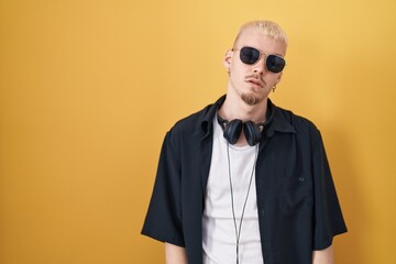 Young caucasian man wearing sunglasses standing over yellow background looking sleepy and tired, exhausted for fatigue and hangover, lazy eyes in the morning.