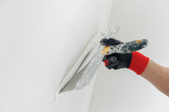 Closeup hands man drywall worker using trowel for plasterer putting stucco on plasterboard white wall