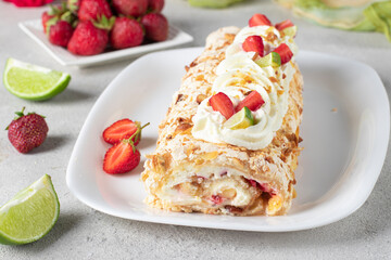 Meringue roll with strawberries and lime on light gray background