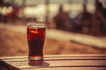 Glass with cola buried in the sand of a beach
