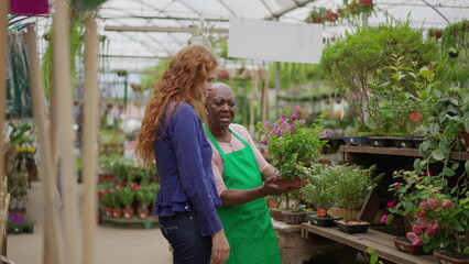 Senior Lady Helping Young Female Client at Local Gardening Shop. An African American elder woman advising customer on plant purchase in a small business Flower Store