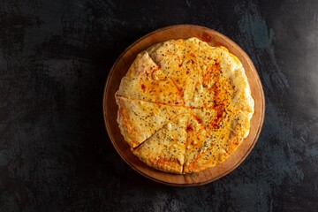 Cheese pizza on black table with abundant yellow cheese