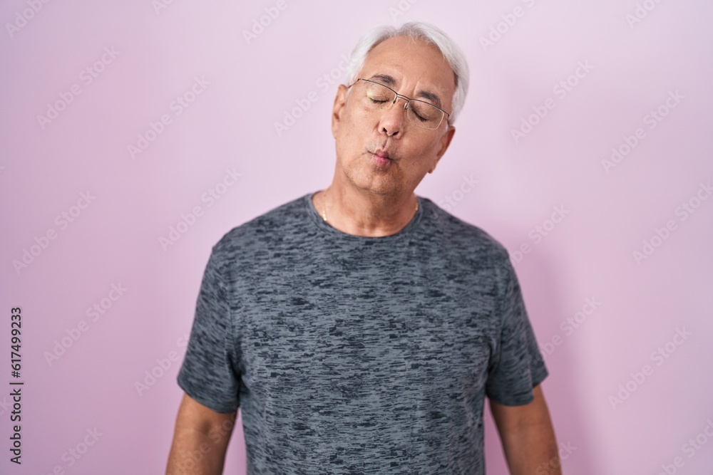 Poster middle age man with grey hair standing over pink background making fish face with lips, crazy and co