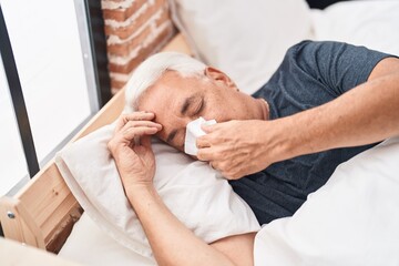 Middle age grey-haired man using napkin lying on bed at bedroom