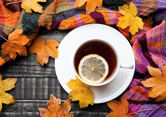 Cup of tea with lemon with scarf and autumn leaves on wooden background