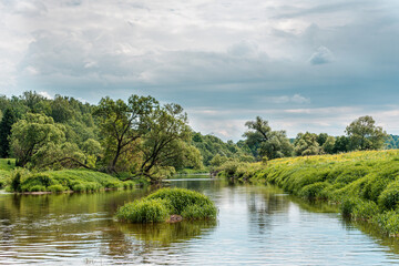 Beautiful green summer landscape of a meadow near a river and a forest. a small river running...