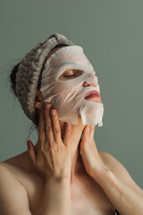 Woman in a fabric mask does skin care. Close-up portrait on a gray background. The beauty industry