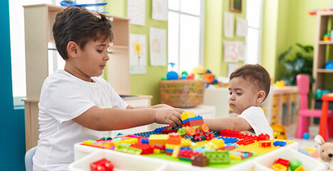 Adorable boys playing with construction blocks sitting on table at kindergarten