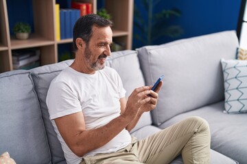 Middle age man using smartphone sitting on sofa at home
