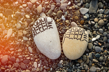 Two traces of the feet made of sea stones, fingers drawn with a marker on background pebbles sea on the beach - 617502469
