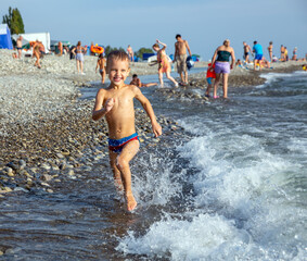 Happy little boy runs along the seashore in the holiday season on the beach - 617502475