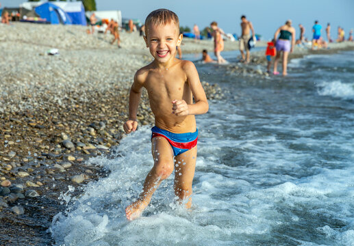 Happy little boy runs along the seashore in the holiday season on the beach
