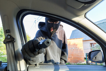 An armed man in the mask threatening pistol to the driver of the car