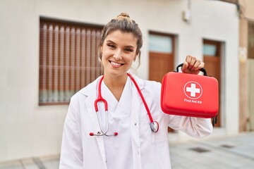 Young doctor woman holding first aid kit looking positive and happy standing and smiling with a...