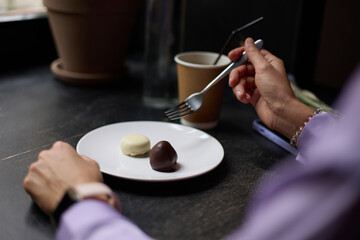 Young woman eating chocolate candies for lunch in a cafe. Unrecognizable female person enjoying sweet treats for snack