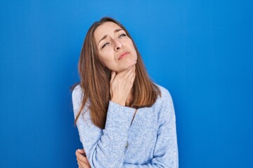 Obraz premium Young woman standing over blue background touching painful neck, sore throat for flu, clod and infection