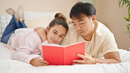 Man and woman couple lying on bed reading book at bedroom