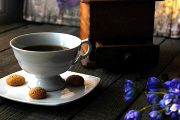 A white cup of coffee with amaretti on the side, blue flowers on the table