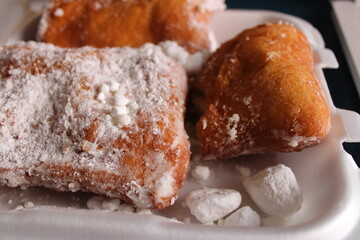 Beignet doughnuts covered in powdered sugar, in takeout container