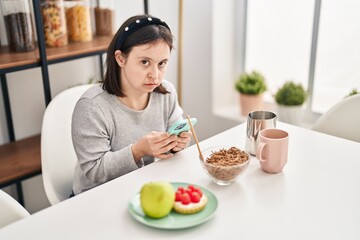 Young woman with down syndrome using smartphone having breakfast at home