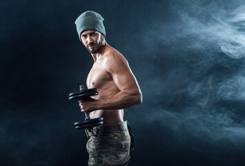 Fototapeta na wymiar Cool confident man with cap lifting weights and working out
