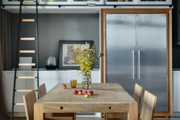 Light wooden table with branches in the vase, apples, glass and  four chairs in the modern kitchen....