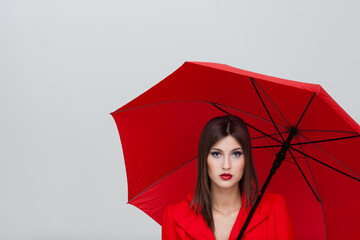 Beautiful young woman with red umbrella posing on grey background