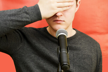 A young man's face covers his eyes with his hand while standing in front of a microphone.  Not...