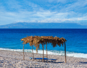 Summer morning pebbly beach with sunbeds and canopy (Albania).