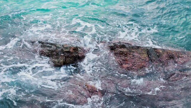 Waves of turquoise sea crash forcefully against rocks creating magnificent sight. Waters of sea are striking in their beauty, power when waves break on rocks and stones giving unforgettable emotions