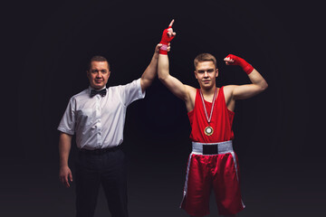 Boxing referee gives medal to young teen boxer in red form and white gloves. Winner. Studio shot on...