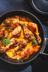 Baked chicken drumsticks with vegetables, casserole dish on black background