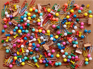 Background of colorful drawing pins, paper clips and metal binder clips on a cork board