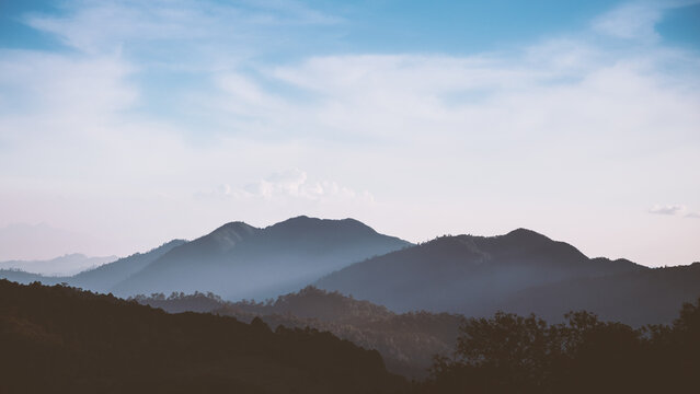Foggy mountain range in low key tone with cloudy blue sky