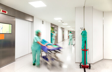 Modern hospital surgery corridor with motion blurred figures of personnel wearing medical uniforms with an emergency bed on wheels.