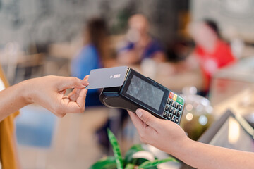 detail of a customer's hand paying the bill with a contactless credit card at a coffee shop in Brazil