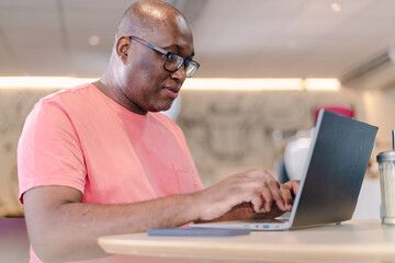 homem Brasileiro negro usando seu computador portátil para acessar a internet em uma cafeteria no...