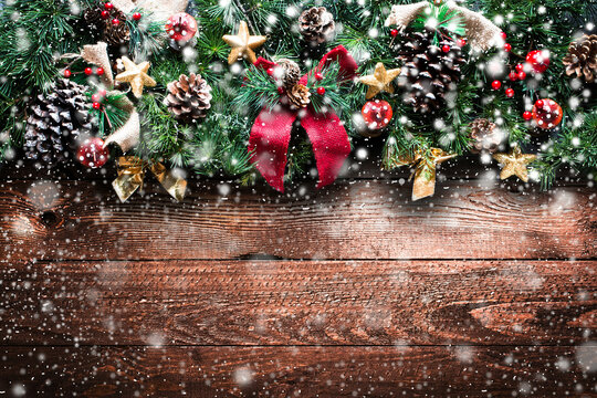 Merry Christmas Frame with Snow and real wood green pine, colorful baubles, knots with berries and other seasonal stuff over an old wooden aged background
