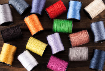 Colorful cotton reels scattered across a dark rustic wooden table