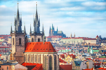Fototapeta na wymiar High spires towers of Tyn church in Prague city (Church of Our Lady before Tyn cathedral) urban landscape panorama with red roofs of houses in old town and blue sky with clouds