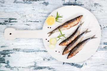 Delicious grilled sardines on wooden kitchen board on white and blue wooden textured background. Culinary seafood eating.