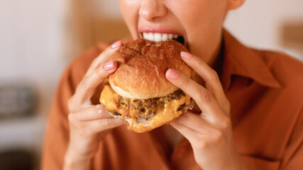 Hungry caucasian woman enjoy eating tasty hamburger, biting home-prepared or delivered junk food meal, closeup, cropped