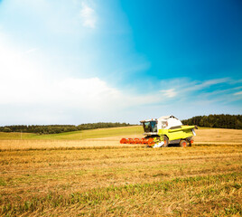 Obraz premium Working Harvesting Combine in the Oat Field. Farmland Background. Agriculture Machinery and Harvest Concept. Harvester Farm Machine. Toned Photo with Copy Space.