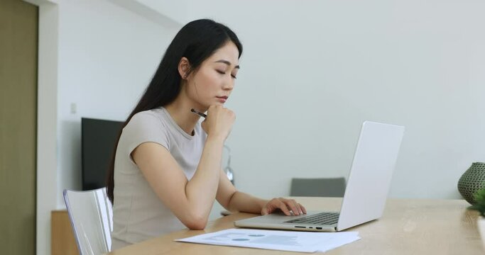 Serious thoughtful Asian student or employee prepare project or assignment, studying seared at desk using laptop, doing research, studying, working at home-office. Workflow with modern tech, analysis