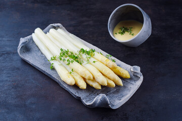 White asparagus glazed with sauce hollandaise and cress served as close-up on a design tray with...