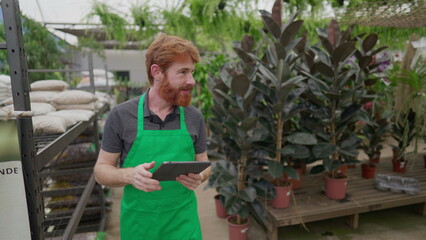 Employee in Green Apron Using Tablet for Inventory While Roaming Flower Shop. Young Man_s Tech-Driven Local Business Operations