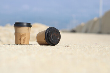 Disposable cardboard cup with plastic lid thrown on the floor. Dirty coffee cup on floor in Mediterranean Sea port. World Environment Day concept idea. Selective focus on disposable cardboard cup. 